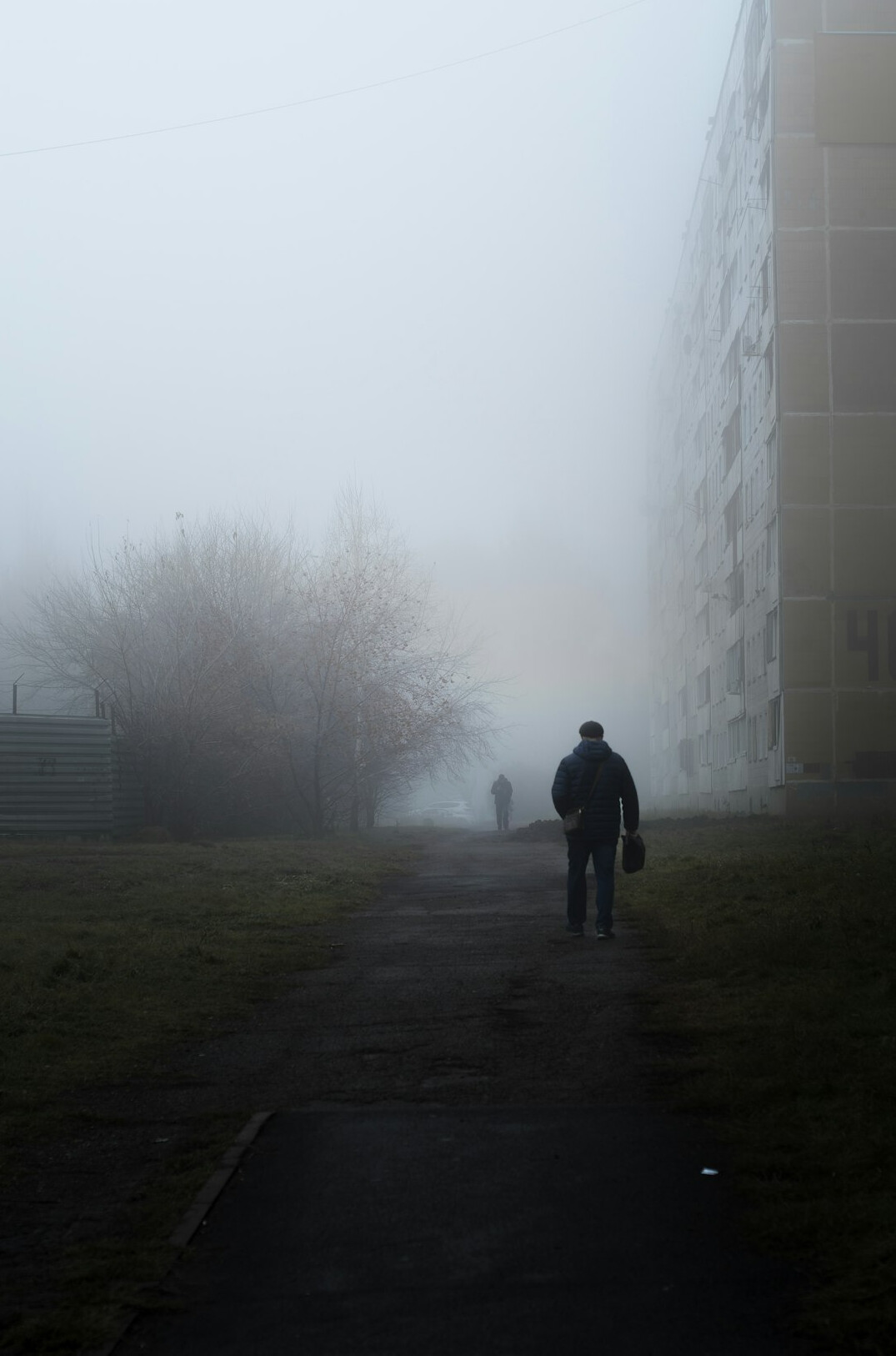 Silhouette of a man in a coat and hat walking down a foggy street